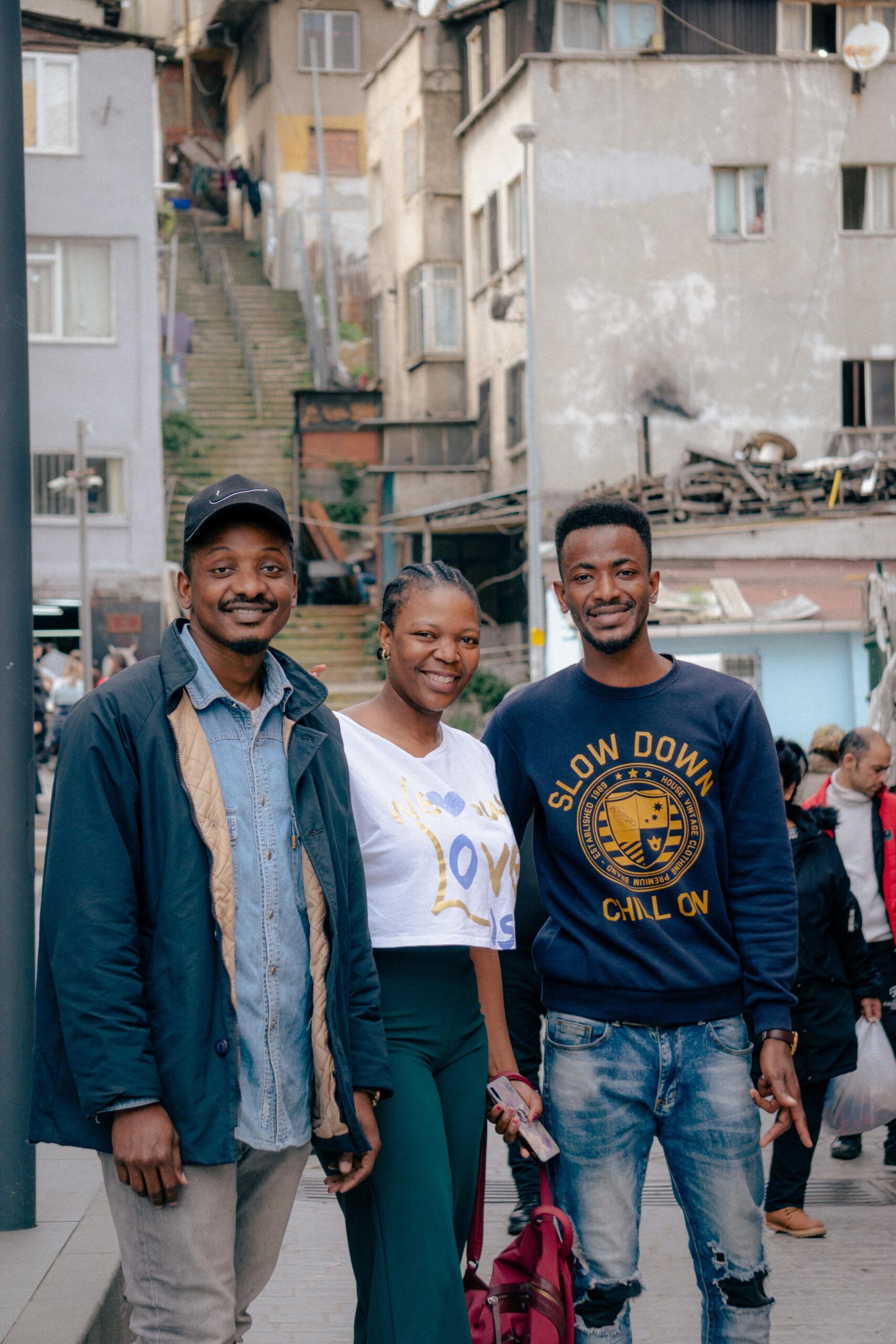A group of three friends posing cheerfully in a bustling old town urban setting with stairs and buildings.